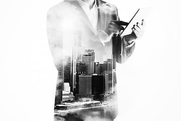 un homme en transparence travaillant sur une tablette, en fond une ville moderne