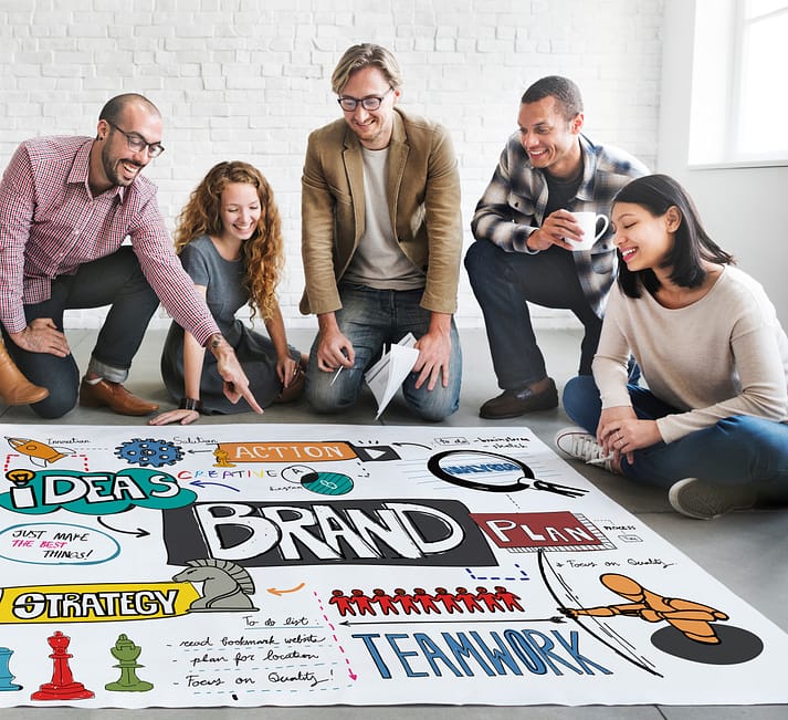 équipe de 5 web designer travaillant à la stratégie de marque et l'identité visuelle d'un client.  grande affiche au sol avec les idées
